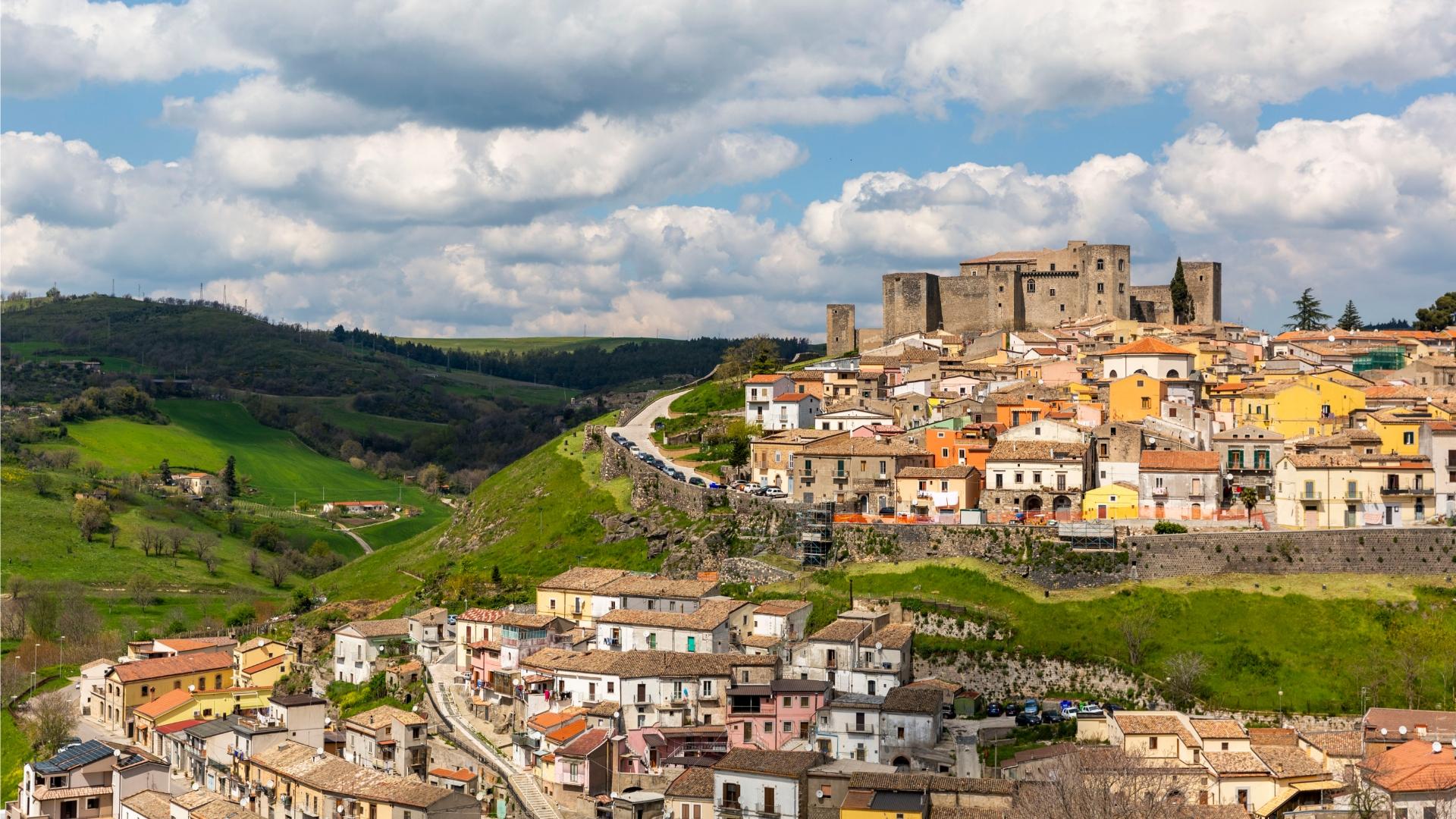 Un borgo pittoresco con un castello su una collina verde sotto un cielo nuvoloso.
