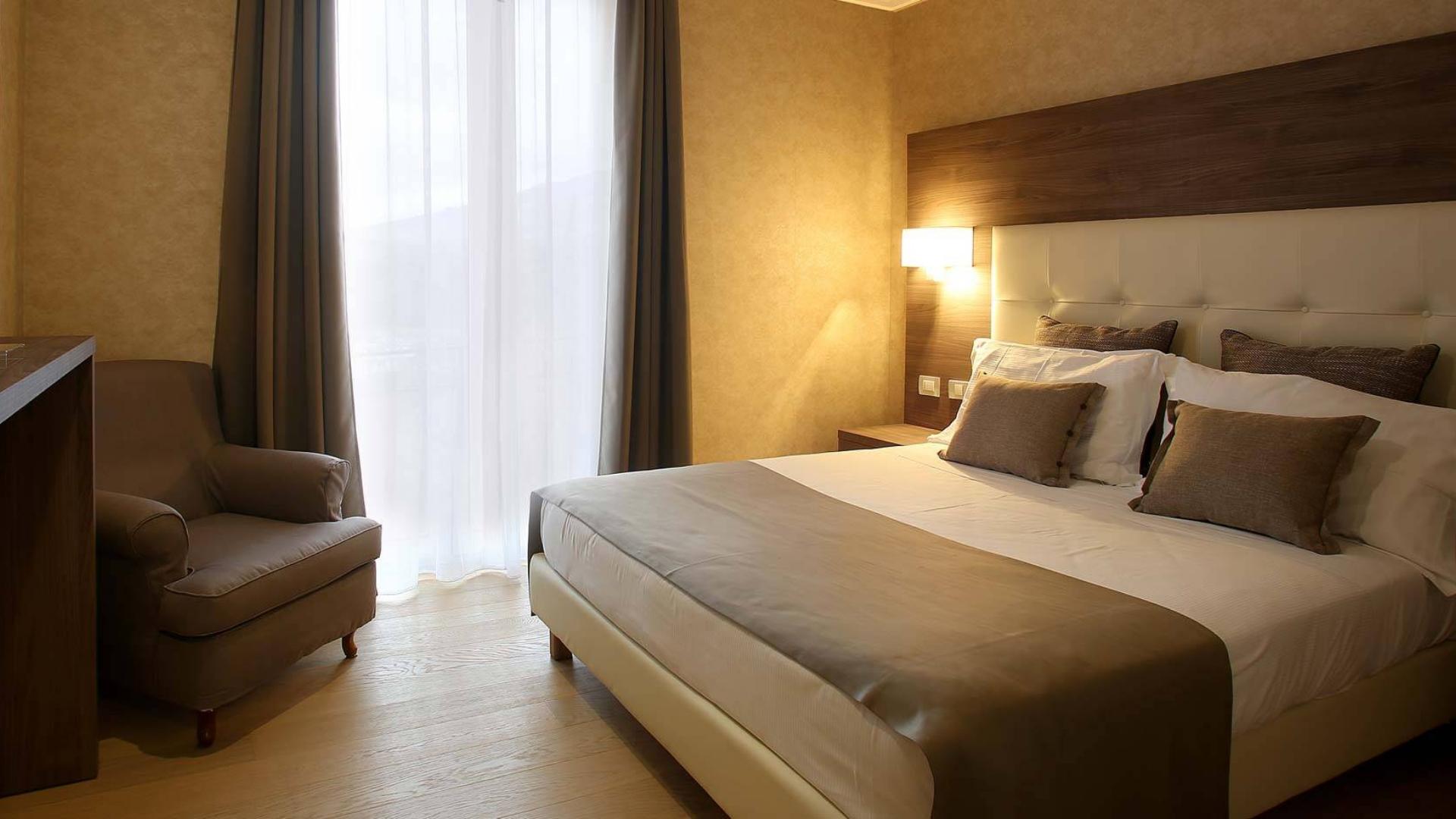 Camera accogliente con letto matrimoniale, poltrona e illuminazione calda.