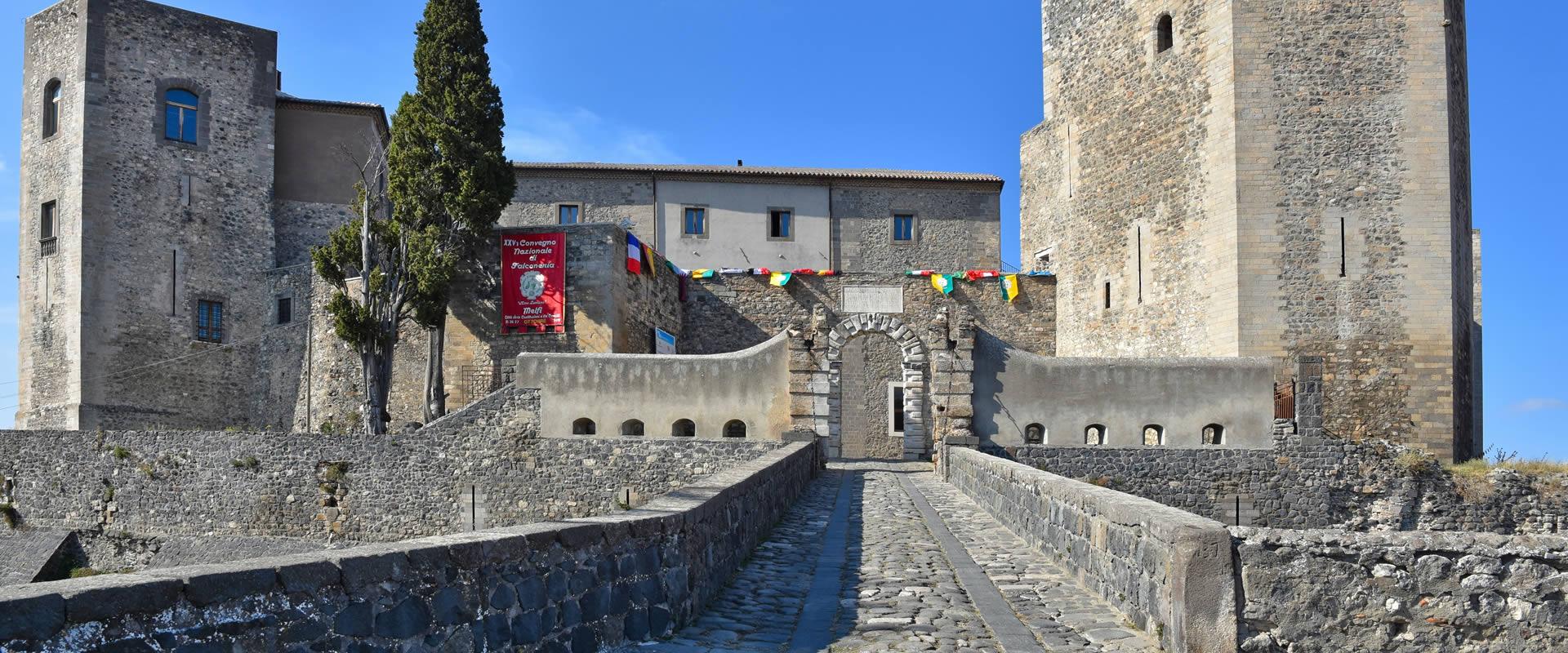 Castello medievale con torri in pietra, ingresso ad arco e bandiere colorate.