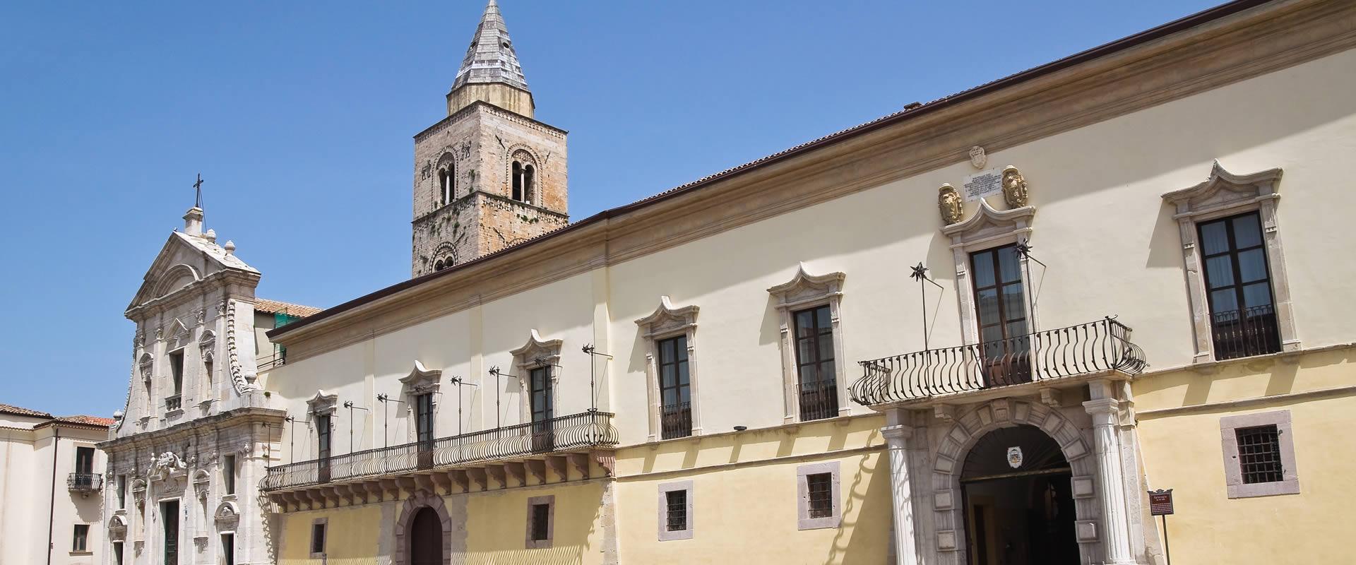 Edificio storico con torre campanaria e facciata barocca sotto un cielo limpido.