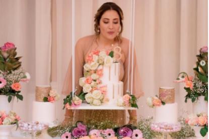 Donna soffia su una torta decorata con fiori, circondata da dolci e fiori.