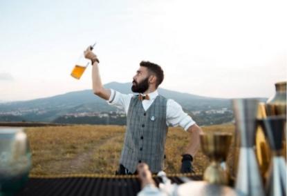 Bartender all'aperto con bottiglia in mano, montagna sullo sfondo.