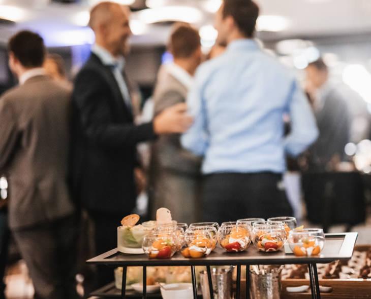 Evento elegante con persone in abiti formali, atmosfera vivace e tavolo con stuzzichini.