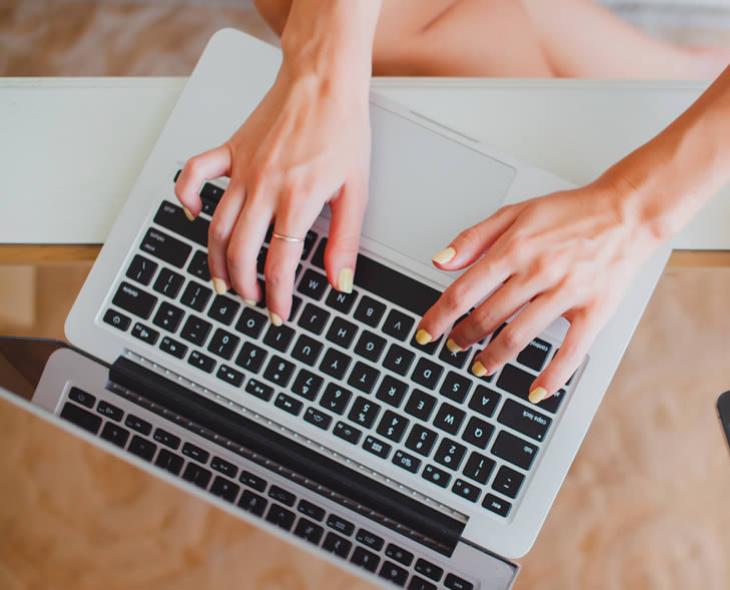 Mani che digitano su un laptop, accanto a un telefono e una tazza di caffè.