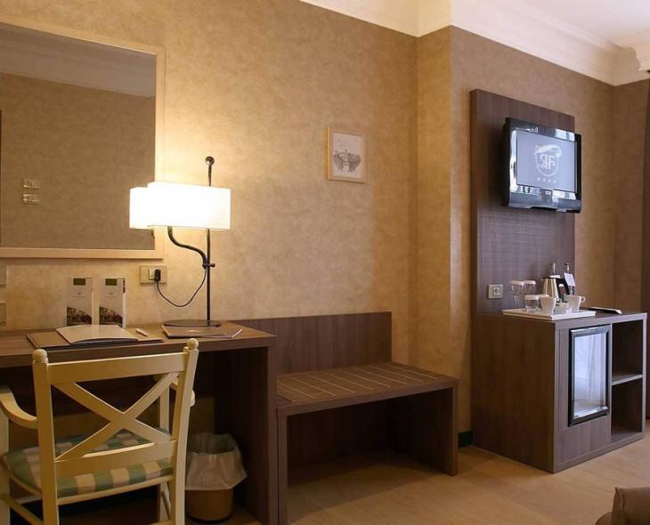 Camera d'hotel con scrivania, sedia, TV, minibar e lampada.