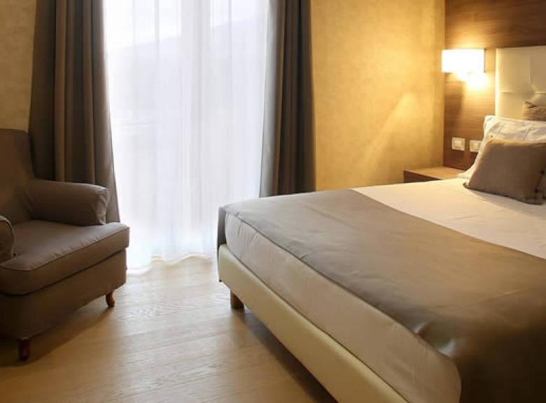Camera elegante con letto matrimoniale, poltrona e illuminazione calda.