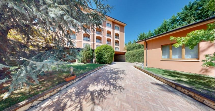 Viale alberato conduce a edificio arancione, atmosfera serena e accogliente sotto cielo limpido.