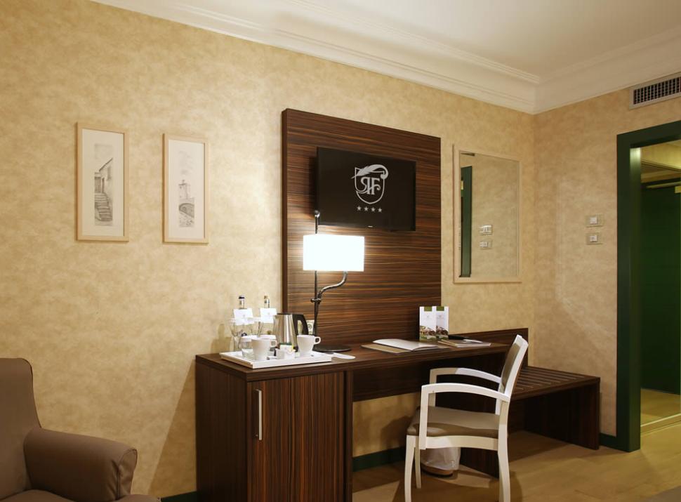 Camera d'hotel elegante con scrivania, lampada, minibar e decorazioni murali.