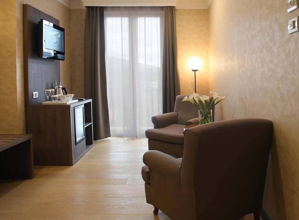 Elegante salotto con poltrone, minibar, TV a parete e lampada da terra.