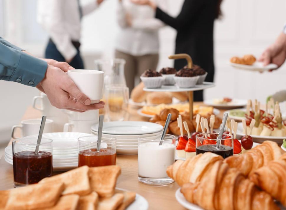 Colazione a buffet con croissant, toast, marmellate e persone che conversano.
