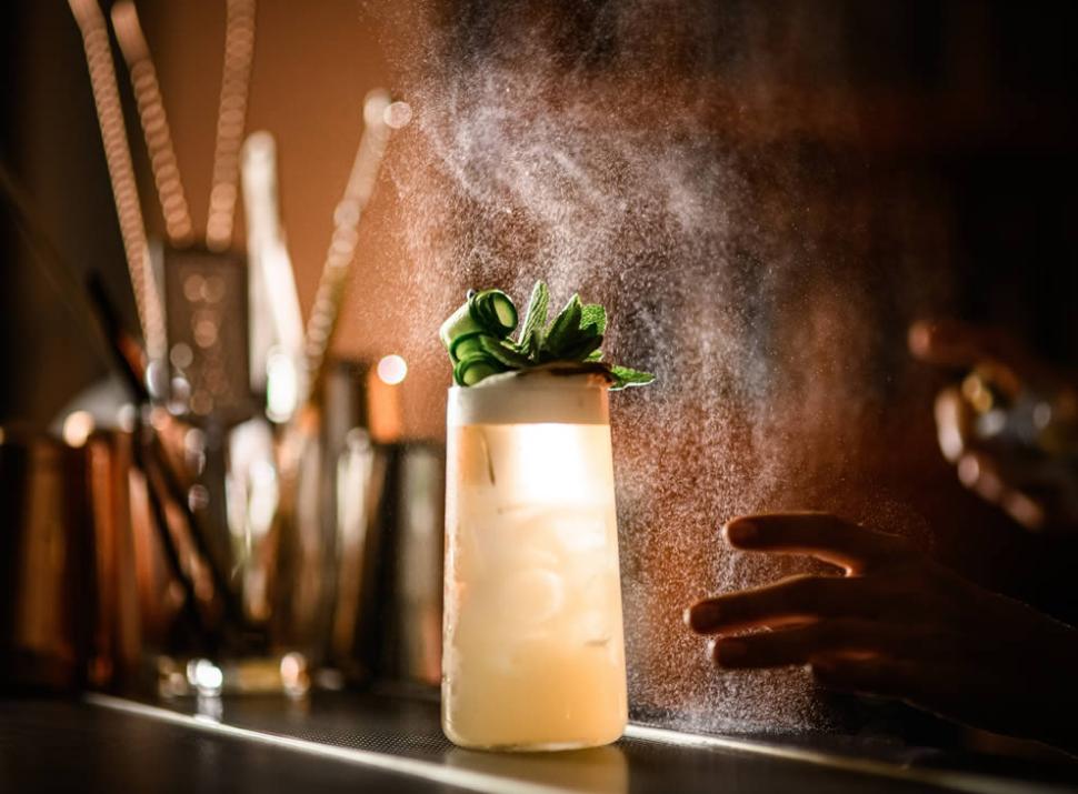 Cocktail elegante con decorazione di erbe, illuminato artisticamente con uno spruzzo di luce.