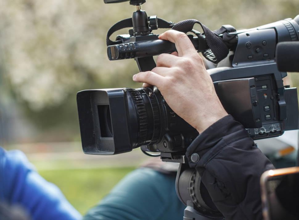 Operatore video che riprende con una telecamera professionale all'aperto.