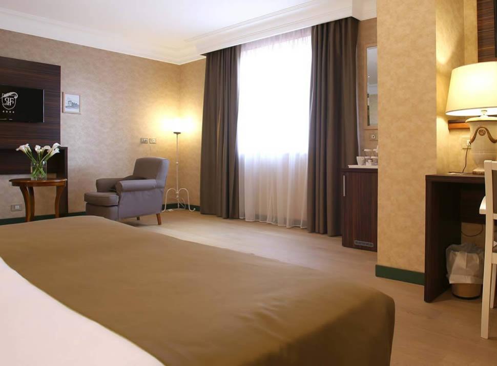 Camera d'albergo elegante con poltrona, scrivania e televisore, decorata in toni caldi.