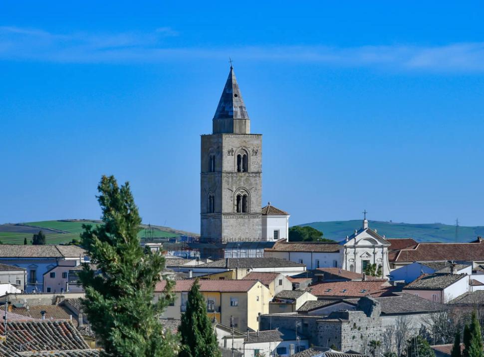 Campanile medievale in un paesaggio urbano con colline sullo sfondo.