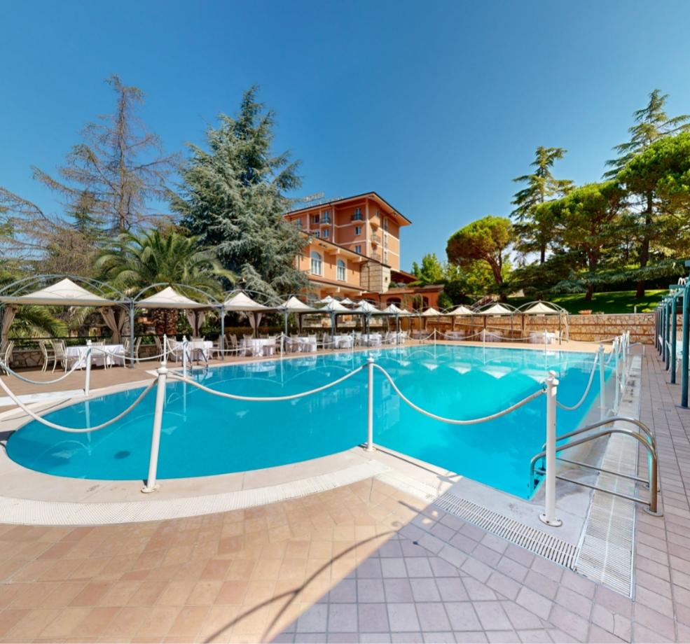 Piscina all'aperto con ombrelloni, immersa nel verde, atmosfera serena e rilassante.